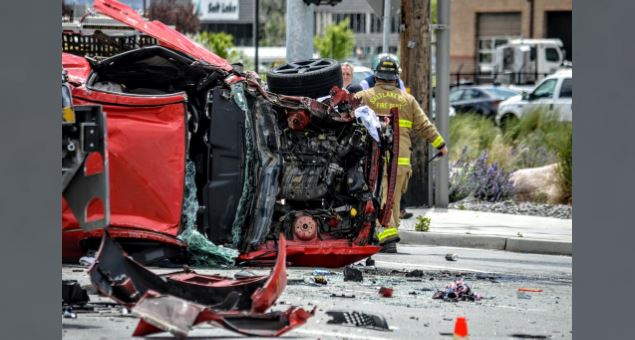 Red car flipped onto its side in a collision with debris on the street; firefighter in turnout gear assesses the scene.