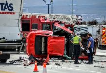 Red SUV overturned on a highway, with emergency responders and fire trucks at the scene, debris scattered nearby.