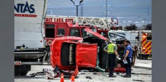 Red SUV overturned on a highway, with emergency responders and fire trucks at the scene, debris scattered nearby.