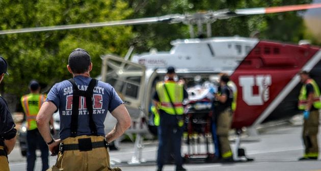 Emergency responders, including firefighters, stand around a stretcher as a medical helicopter is on site for evacuation nearby.