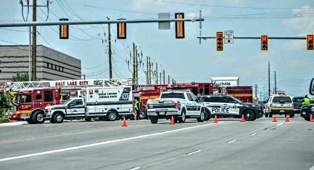 Emergency responders block a city intersection with fire trucks, an ambulance, a police car, and orange cones.
