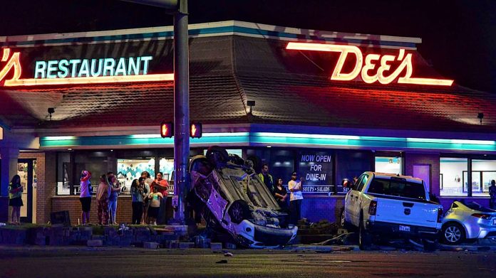 Mukti-vehicle crash Redwood Rd and 4700 South in Taylorsville Overturned white car on the sidewalk in front of a neon-lit diner at night, with a crowd watching the crash scene.