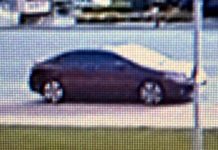 Side profile of a dark sedan parked on a street, viewed from the curb side in daylight