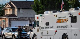 Davis County Sheriff mobile command center emergency vehicle parked on a suburban street, a deputy speaks on a radio beside a silver SUV.