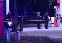 Man shot, killed at Taylorsville gas station; police search for shooter Police officers stand behind yellow caution tape at a dimly lit gas station scene, documenting evidence at night.