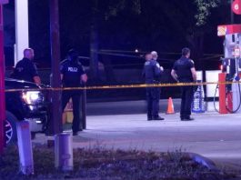 Man shot, killed at Taylorsville gas station; police search for shooter Police officers stand behind yellow caution tape at a dimly lit gas station scene, documenting evidence at night.