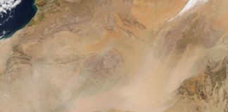Aerial view of a sandy desert with a broad dust cloud sweeping across the landscape