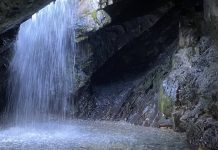Teen airlifted after fall above Donut Falls in Big Cottonwood Canyon Waterfall spilling from a rocky cave ceiling into a small pool among dark jagged walls.