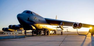 A large military bomber parked on a sunlit runway with ground crew nearby at dusk. erial vehicle ready on tarmac at sunset.