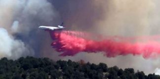 Air tanker drops red fire retardant over a forest fire with dark smoke in the background used to slow flames and protect trees.