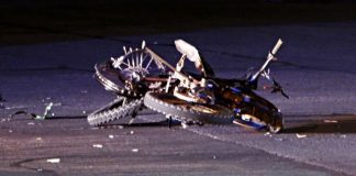 Bicycle crashed on a dark road at night; bike on its side with a bent wheel and scattered debris around it.