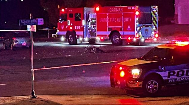 Nighttime emergency scene with a red Herriman Fire Authority fire truck and a marked police SUV with lights on, at a street intersection.
