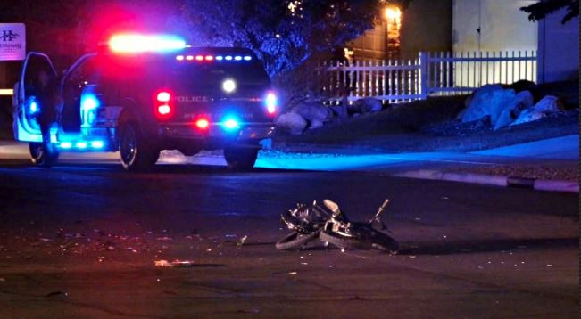 Police SUV with flashing red and blue lights at night; a damaged bicycle lies on the wet street in the foreground.