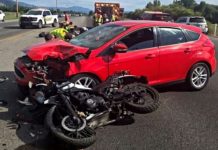 Motorcyclist transported to hospital after Logan collision Red hatchback with severe front-end damage after a collision with a black motorcycle; emergency responders at the scene on a highway.
