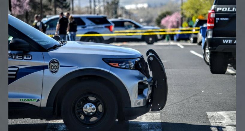 Police SUV in the foreground with a push bumper, at a cordoned-off street with yellow tape and officers in the background.