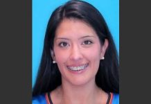 Portrait of a smiling woman with long dark hair, braces, and pearl earrings against a bright blue background.
