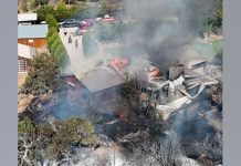 Residential area on fire: burning houses with thick smoke rising above a yard and surrounding trees.