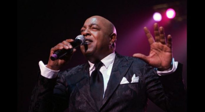 Peabo-Bryson-singer-known-for-Disney-hits-dies-at-75-after-stroke Male singer in a dark suit performs on stage, microphone in hand, pink spotlight behind him.