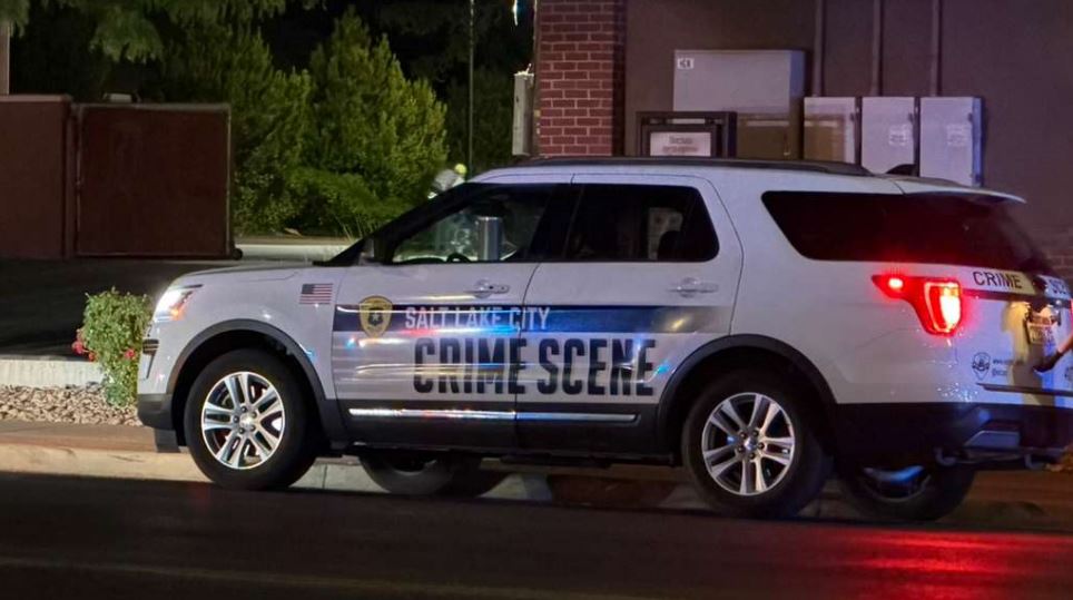 White crime scene SUV with blue stripe parked on a street at night its markings and red taillights visible under streetlights