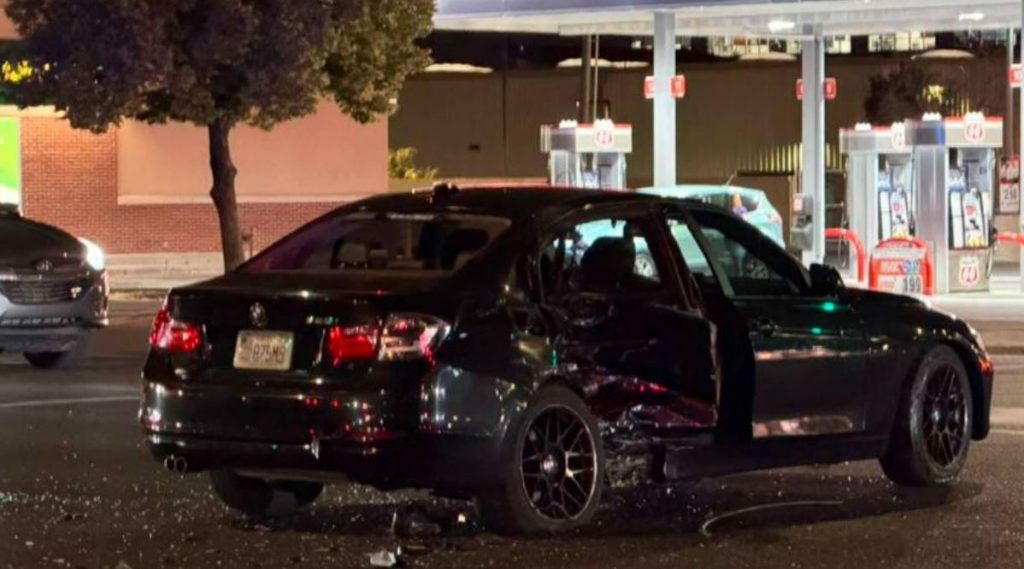 Black sedan with major damage to the right side parked at a gas station at night debris on the ground nearby