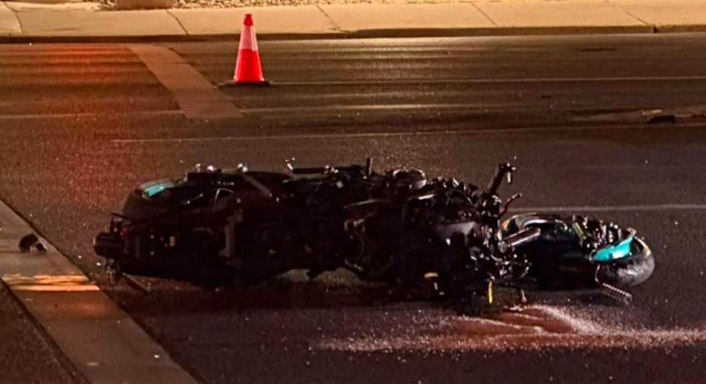 Motorcycle wreck on a wet street at night with a traffic cone in the background and debris scattered nearby