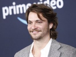 Smiling man with medium-length brown hair and light beard wearing a gray blazer and white shirt at a Prime Video event.