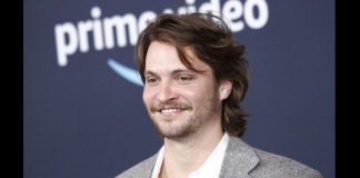 Season 2 of Luke Grimes’ ‘Marshals’ now filming in Park City Smiling man with medium-length brown hair and light beard wearing a gray blazer and white shirt at a Prime Video event.