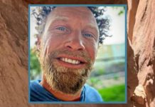 Close-up portrait of a smiling man with a light beard outdoors.