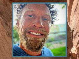 Close-up portrait of a smiling man with a light beard outdoors.