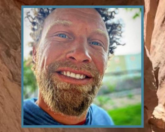Close-up portrait of a smiling man with a light beard outdoors.