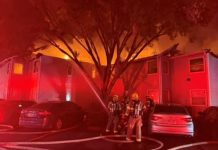 Multiple residents displaced by St. George apartment fire Firefighters in gear stand outside a smoke-filled, multi-unit building at night as flames glow red; cars are parked nearby and hoses cover the ground.