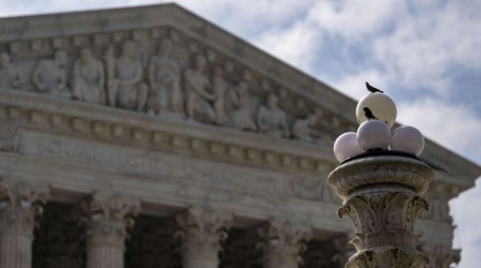 Supreme-Court-strikes-down-coordinated-campaign-finance-limits Ancient temple façade with carved frieze and columns, viewed behind a decorative fountain topped with white spheres and two pigeons perched on them.