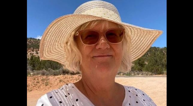Woman on a sunny beach wearing a wide-brim straw hat and sunglasses, smiling slightly.
