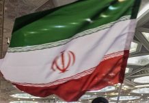 Iranian flag draped indoors at an event, green white red with the emblem in the white band, hanging in a hall.
