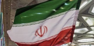 Iranian flag draped indoors at an event, green white red with the emblem in the white band, hanging in a hall.