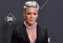 Woman with short silver hair in a black blazer and pink ruffled blouse posing on the red carpet at the People’s Choice Awards.
