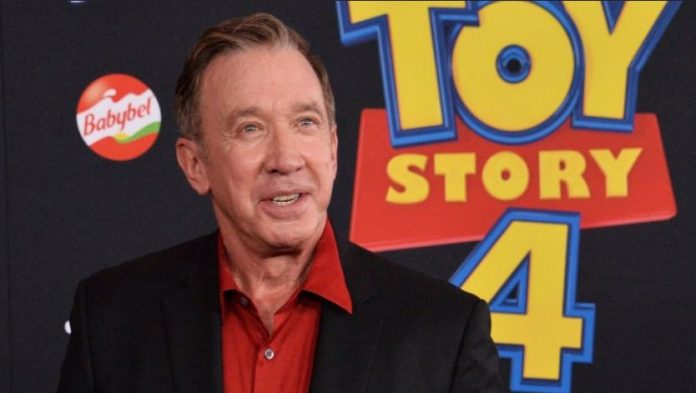 Toy-Story-5-tops-North-American-box-office-with-70M Smiling man in a red shirt and black blazer standing in front of a Toy Story 4 backdrop with a Babybel logo visible on the left.
