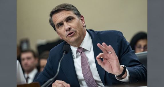 Trump-administration-seeking-to-denaturalize-17-over-offenses Man in a blue suit speaks into a microphone during a formal hearing, gesturing with his right hand.