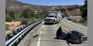 Motorcycle lying on its side in a rural two-lane highway; an ambulance and another vehicle stopped nearby with desert hills in the background.