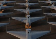 Row of white military-style jet aircraft parked in neat rows on a tarmac, viewed from above at sunset/low light.