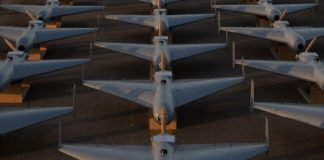 Row of white military-style jet aircraft parked in neat rows on a tarmac, viewed from above at sunset/low light.