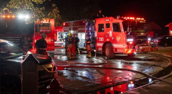 Firefighters and red fire trucks at night, hoses on the wet street preparing for operation.