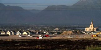 Town under mountains with a construction site and several parked cars in the foreground.