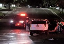 Nighttime accident scene: a white SUV with open doors beside a police SUV with flashing red lights; responders in reflective vests assist nearby.