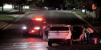 Nighttime accident scene: a white SUV with open doors beside a police SUV with flashing red lights; responders in reflective vests assist nearby.