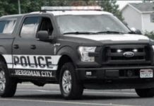 Police pickup truck with 'POLICE' and 'HERRIMAN CITY' markings driving on a street, emergency lights on the roof.