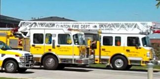 Two yellow Clinton Fire Department ladder trucks with extended ladders parked side by side on a street.