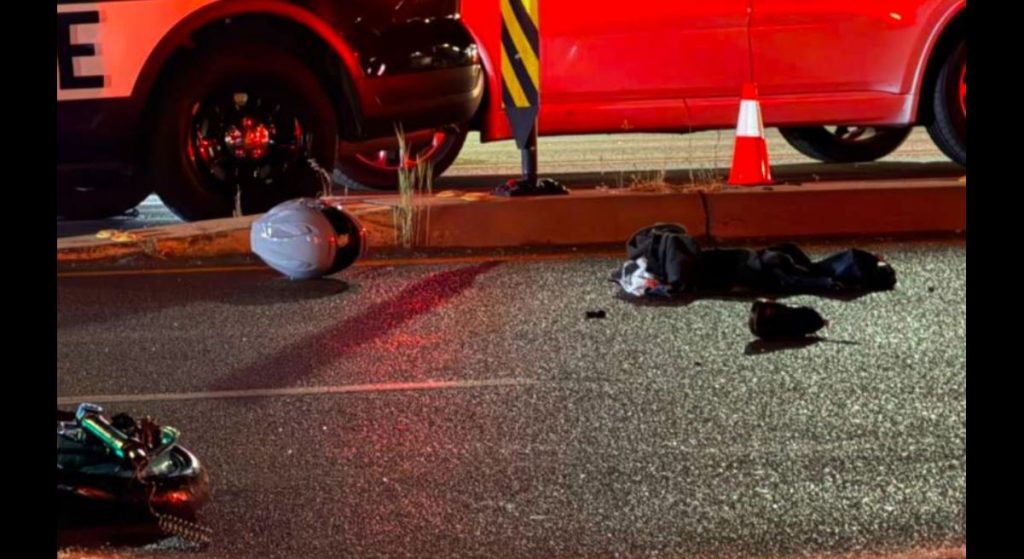 Nighttime crash scene on a roadway a white helmet dark clothing and debris near a red car and cone