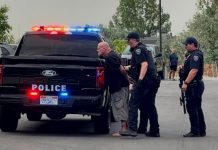 Man in custody after allegedly firing gun in Bluffdale hotel room when police responded Arrest scene: two police officers detain a barefoot man near a black police pickup with flashing red and blue lights in a parking lot.