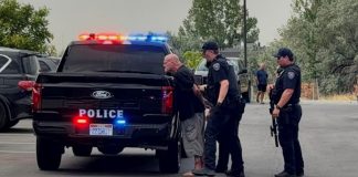 Arrest scene: two police officers detain a barefoot man near a black police pickup with flashing red and blue lights in a parking lot.